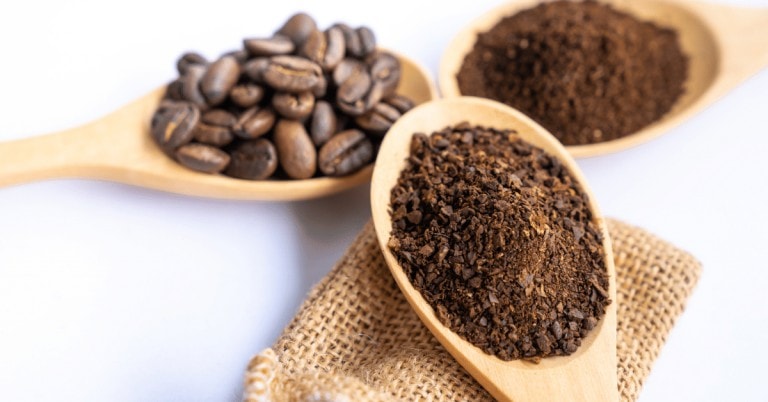 ground and whole coffee beans on wooden spoons