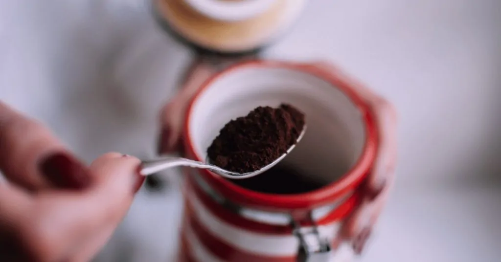 woman holding coffee jar and spoon with ground coffee