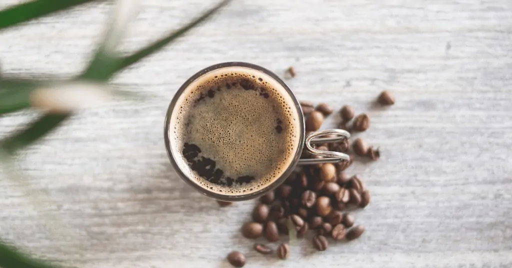 cup of black coffee with coffee beans around it