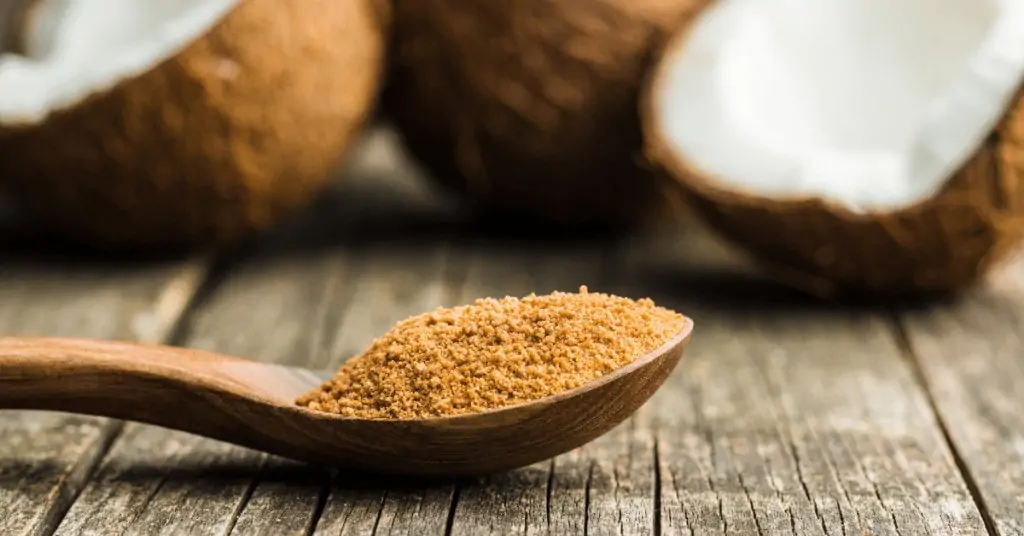 coconut sugar on a spoon with coconuts in the background