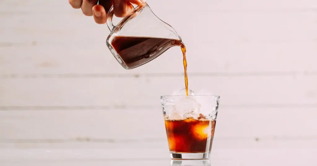 person pouring cold brew into a glass over ice