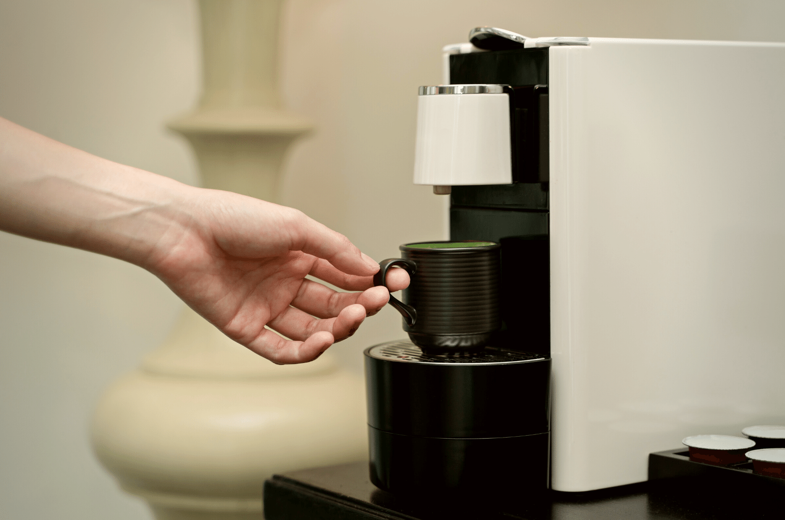 a person holding cup on coffee maker